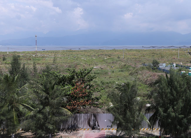 Hình ảnh một góc Khu đô thị lấn biển Đa Phước nhìn từ trên cao với khu đất trống rộng rãi, cỏ mọc um tùm, phía trước là biển 