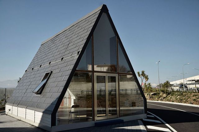 Hình ảnh toàn cảnh một ngôi nhà gấp đã hoàn thiện với cấu trúc chữ A, mái xám, cửa kính trong suốt