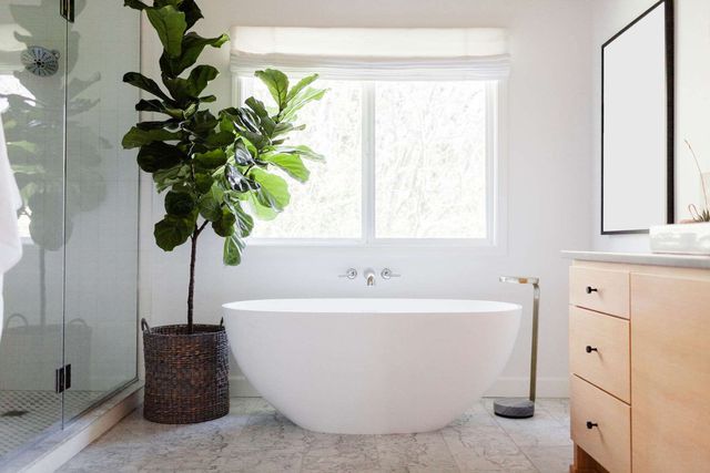 Hình ảnh một góc phòng tắm màu trắng được trang trí bởi chậu cảnh xanh tốt trồng trong chậu mây, cạnh đó là tủ gỗ lưu trữ