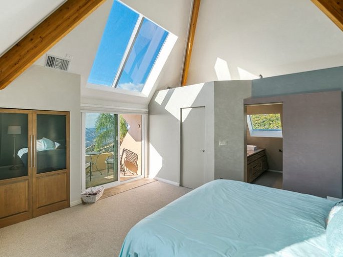 Hình ảnh phòng ngủ trên tầng 2 được bài trí đơn giản, giường nệm màu trắng sáng, cửa sổ kính, mở ra ban công thư giãn