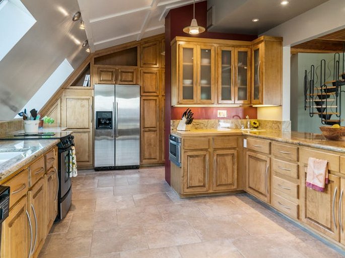 Hình ảnh một phòng bếp với hệ tủ lưu trữ bằng gỗ tự nhiên màu sáng, tủ lạnh xám, cửa sổ kính trong suốt