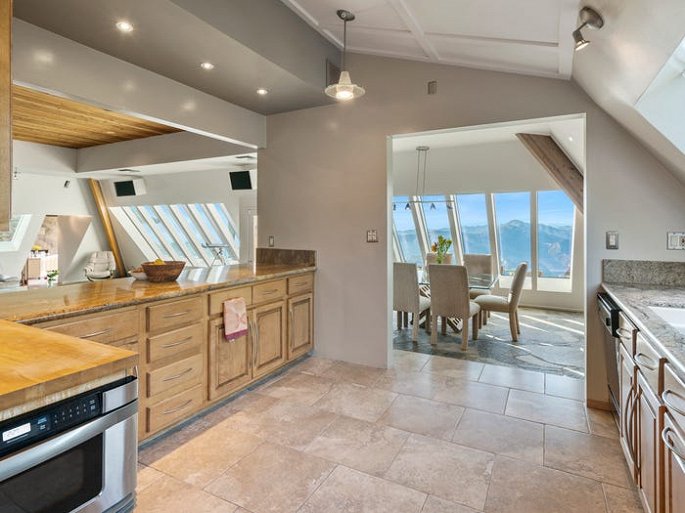 Hình ảnh phòng bếp với tủ bếp bằng gỗ tự nhiên, cửa sổ kính, nhìn ra khu vực bàn ăn bên ngoài