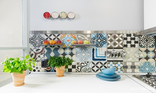 Hình ảnh một góc phòng bếp với mảng tường ốp gạch bông màu sắc, trên bệ bếp là hai chậu cảnh xanh mướt và bộ cốc màu xanh dương