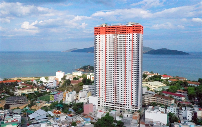 Hình ảnh một tòa nhà cao tầng màu trắng, đỏ cam nổi bật giữa khu dân cư thấp tầng, hướng nhìn ra biển