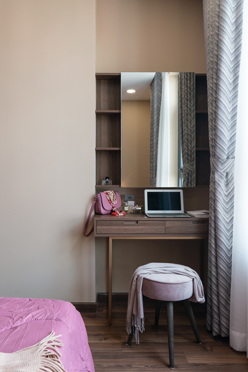 Hình ảnh cận cảnh một góc phòng ngủ với bàn trang điểm bằng gỗ tích hợp chức năng làm việc, ghế ngồi bọc nệm màu tím, rèm cửa xám