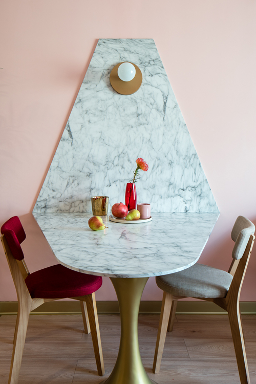 Hình ảnh cận cảnh bàn ăn gắn tường với bề mặt đá cẩm thạch trắng, phần chân mạ vàng, ghế ăn tông màu lãng mạn