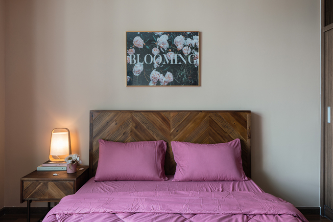 Hình ảnh phòng ngủ được bài trí đơn giản với giường gỗ mộc mạ, ga gối màu tím, đèn bàn, trang trang trí đầu giường