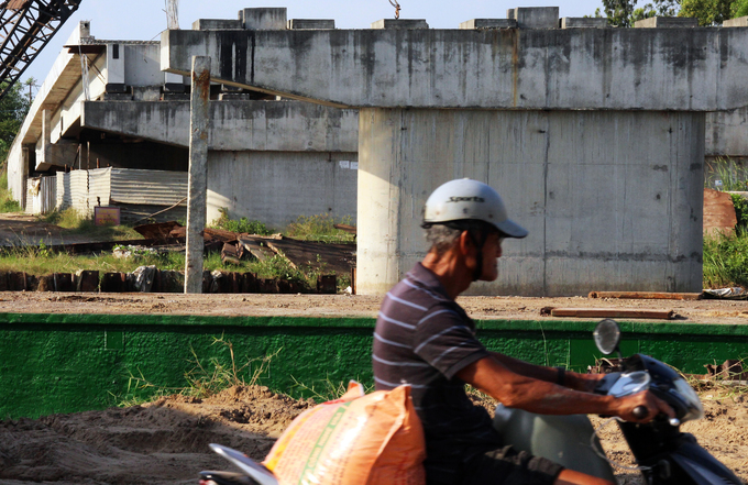 Hình ảnh một người đàn ông lớn tuổi đi xe máy qua công trình cầu xây dở