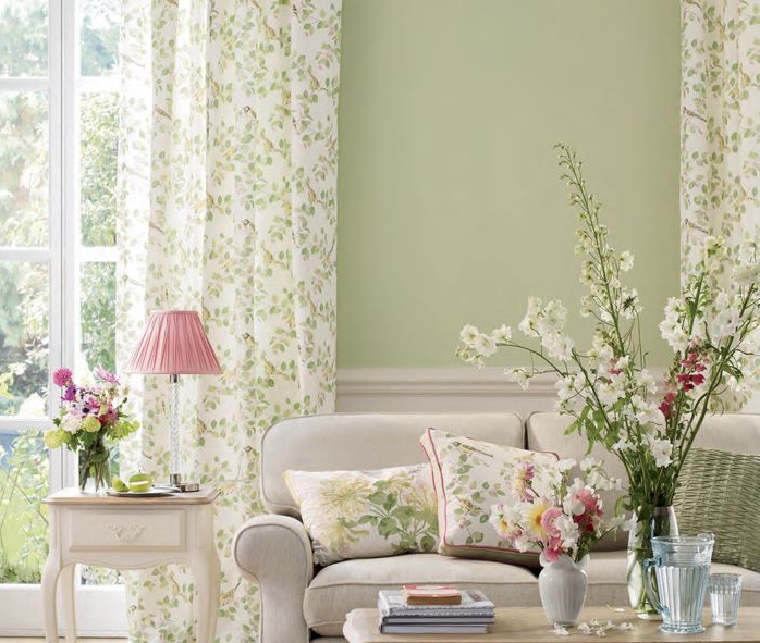 Hình ảnh một góc phòng khách với ghế sofa trắng, rèm cửa sổ kính màu trắng, họa tiết lá xanh nhẹ nhàng