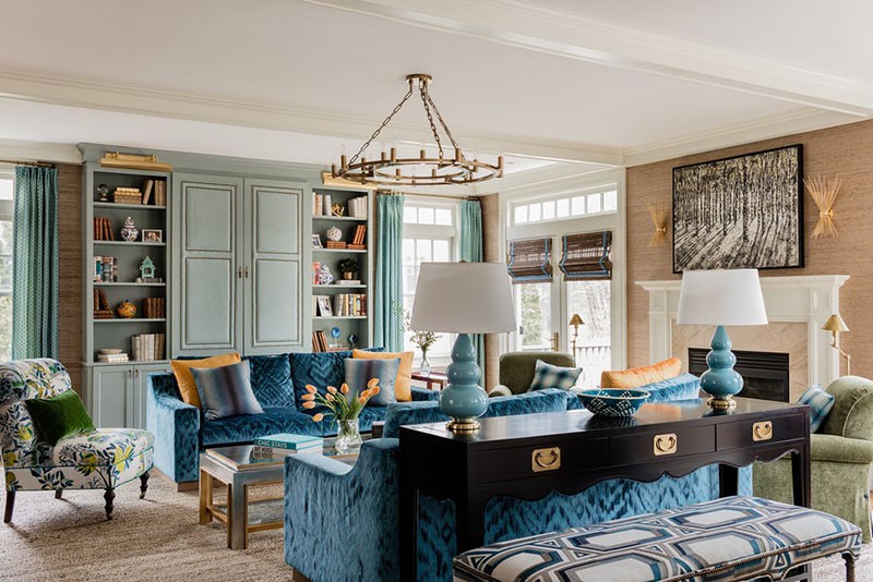 Hình ảnh toàn cảnh phòng khách với ghế sofa xanh dương bài trí đối xứng nhau qua bàn trà, cạnh đó là ghế bành thư giãn họa tiết hoa lá, tủ kệ lưu trữ màu xanh lam, đèn chùm trang trí