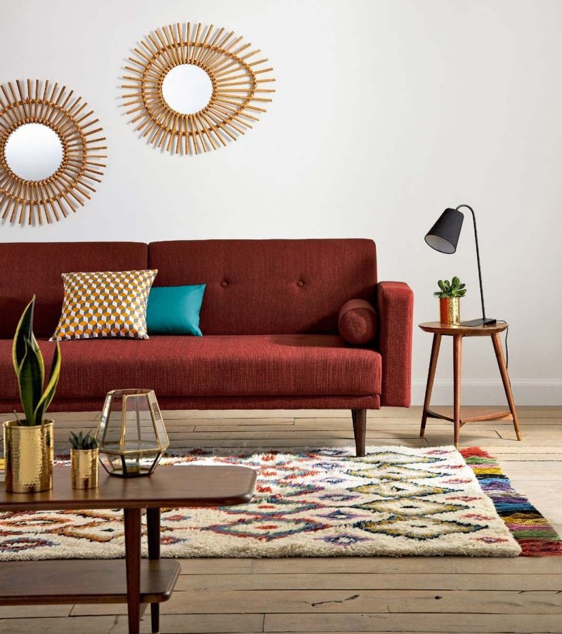 Hình ảnh cận cảnh một góc phòng khách ngày Tết với sofa màu đỏ đô, thảm trải sợi bông mềm mại, tường trang trí hình mặt trời, chậu cây lô hội, bàn trà gỗ