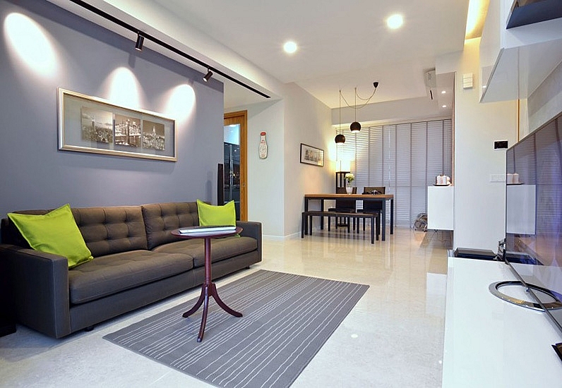 Hình ảnh phòng khách hiện đại với ghế sofa ghi xám, gối tựa màu xanh lá, tranht reo tường, thảm trải, bàn trà, liền kề là phòng bếp ăn