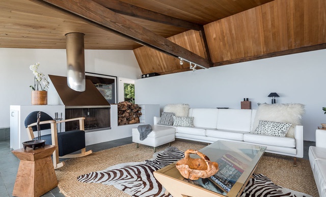 Hình ảnh phòng khách với sofa trắng, lò sưởi, trần gỗ, gầm gỗ, thảm trải họa tiết ngựa vằn
