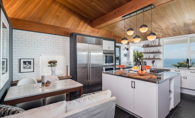 Hình ảnh toàn cảnh phòng bếp hiện đại với hệ tủ kệ màu trắng, trần ốp gỗ, bàn ăn trong góc phòng