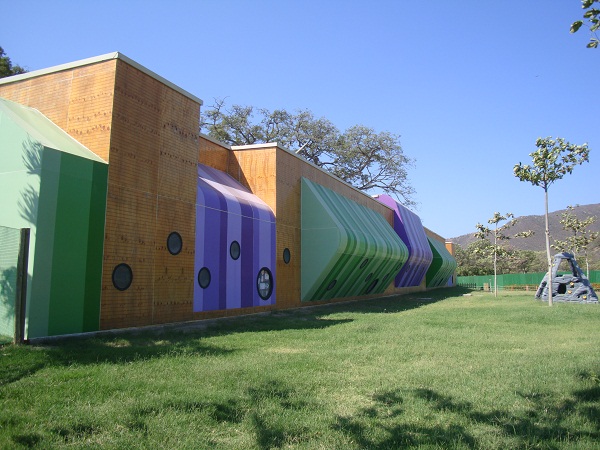 Hình ảnh một mặt bên của công trình trường học với những khối màu sắc rực rỡ gồm tím, xanh lá, vàng gỗ