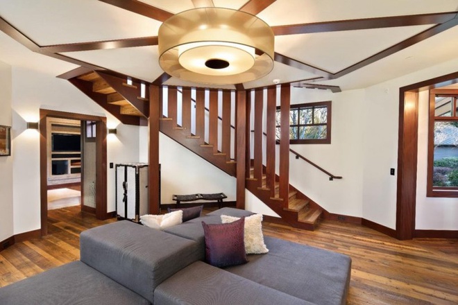 Hình ảnh bên trong biệt thự với sofa phòng khách màu xám, cạnh đó là cầu thang gỗ, đèn chùm trang trí