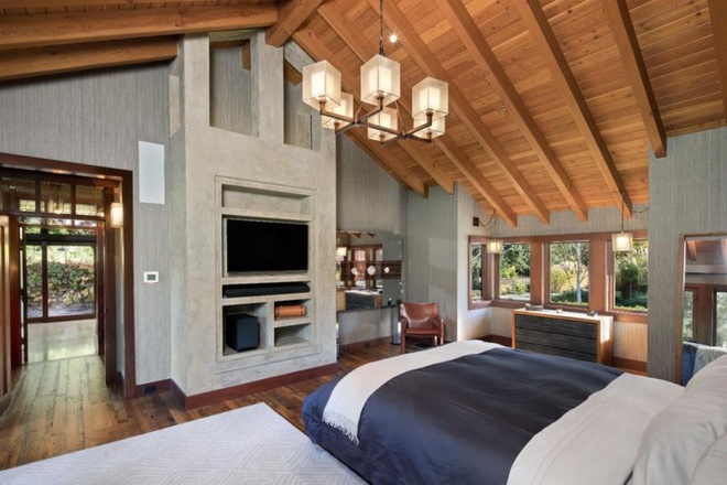 Hình ảnh không gian phòng ngủ được thiết kế với trần nhà cao ốp gỗ, lò sưởi ấm áp, những ô cửa kính mở ra sân vườn xanh mướt bên ngoài.