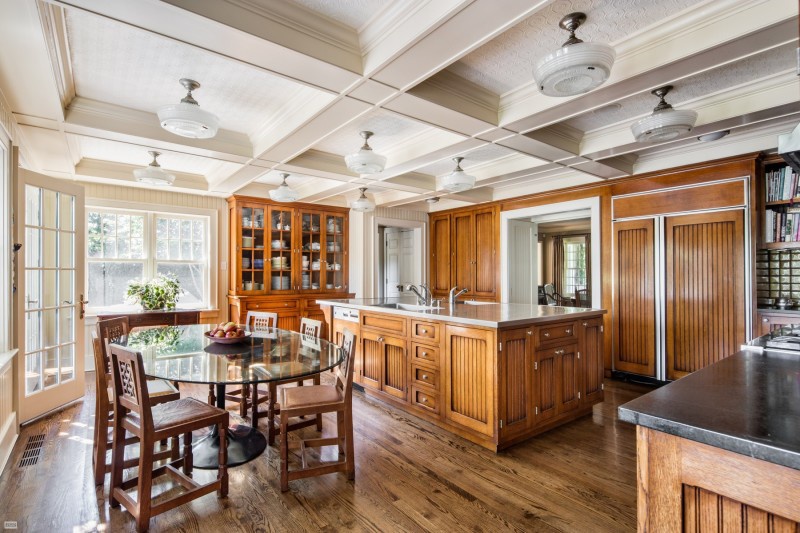 Hình ảnh toàn cảnh một phòng bếp rộng với tủ kệ làm bằng gỗ tự nhiên, trần nhà màu trắng, sàn lát gỗ, cạnh đó là bàn ăn hình tròn lớn, cửa kính trong suốt