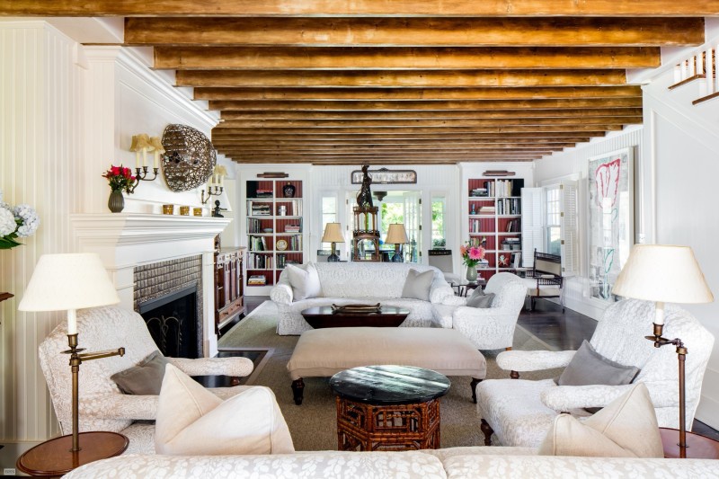 Hình ảnh một phòng khách có trần dầm gỗ tự nhiên, sofa màu trắng, bàn trà hình trụ, lò sưởi ấm áp
