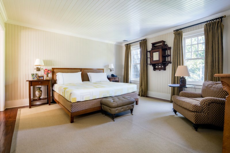 Hình ảnh bên trong một phòng ngủ phụ với tường, trần ốp thanh gỗ màu trắng, rèm cửa màu vàng nhạt, giường nệm đơn giản, tủ kệ gỗ