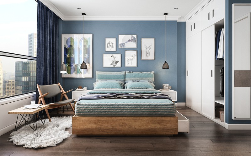 Hình ảnh phòng ngủ thoáng sáng với giường gỗ tự nhiên, tường đầu giường sơn xanh, treo tranh, rèm cửa xanh than, bàn ghế thư giãn, đọc sách
