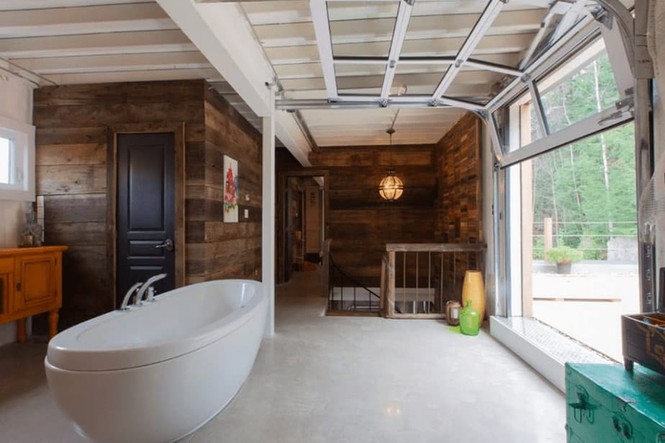 Hình ảnh cận cảnh bồn tắm bằng sứ màu trắng trong phòng ngủ, cạnh đó là khung cửa kính trong suốt, cửa gỗ, cầu thang lên xuống