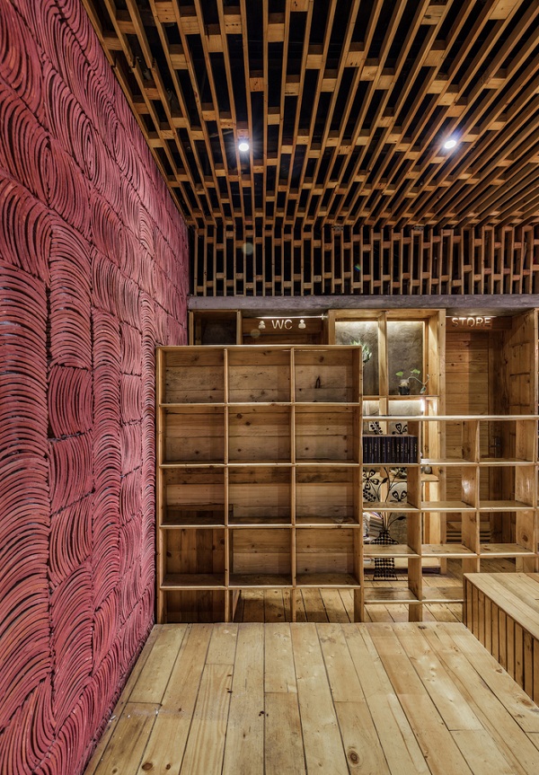 Hình ảnh cận cảnh một căn phòng bên trong quán cà phê với tường trang trí màu hồng tím, trần gỗ, tủ kệ gỗ chia làm nhiều ngăn