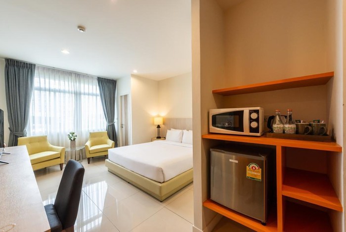Hình ảnh một phòng nghỉ trong khách sạn với giường nệm màu trắng, ghề sofa vàng đặt cạnh cửa sổ kính trong suốt