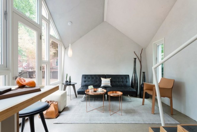 Hình ảnh một phòng khách màu trắng chủ đạo với trần cao, cửa sổ kính, sofa da màu đen, bàn trà tròn, cạnh đó là khu bếp ăn