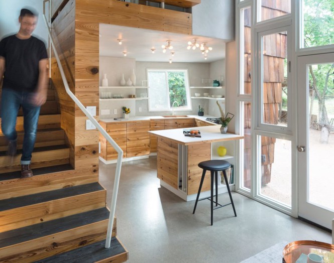 Hình ảnh cận cảnh một người đàn ông đang bước xuống cầu thang gỗ, cạnh đó là phòng bếp hiện đại, đầy đủ tiện nghi