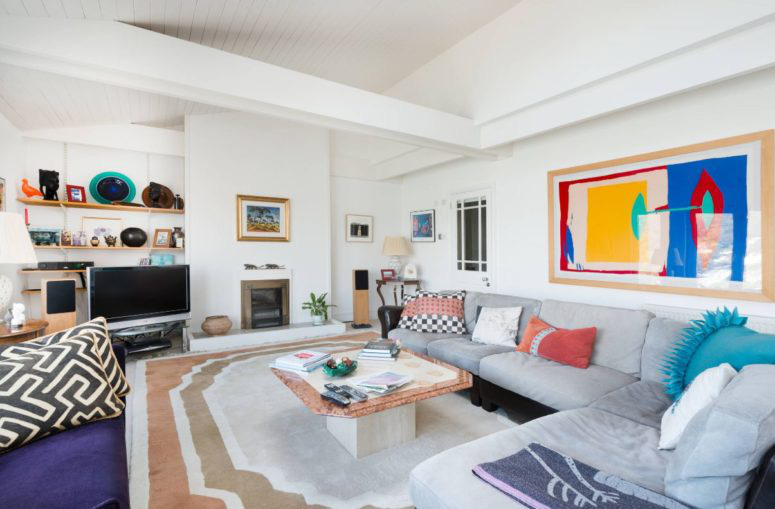 Hình ảnh một phòng khách rộng rãi với tường, trần màu trắng, sofa xám, điểm nhấn là tranh treo tường và gối tựa màu sắc