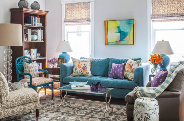 Hình ảnh một phòng khách rực rỡ sắc màu với ghế sofa xanh dương, bàn trà kính chữ nhật, ghế thư giãn bọc nỉ hoa, tủ sách bằng gỗ