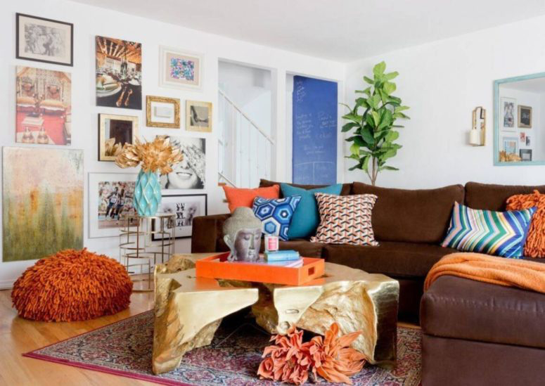Hình ảnh toàn cảnh một phòng khách với bộ ghế sofa màu gỉ sét phối kết hài hòa với bàn trà ánh kim, tranh treo tường, thảm trải họa tiết thổ cẩm, chậu cảnh xanh mướt...