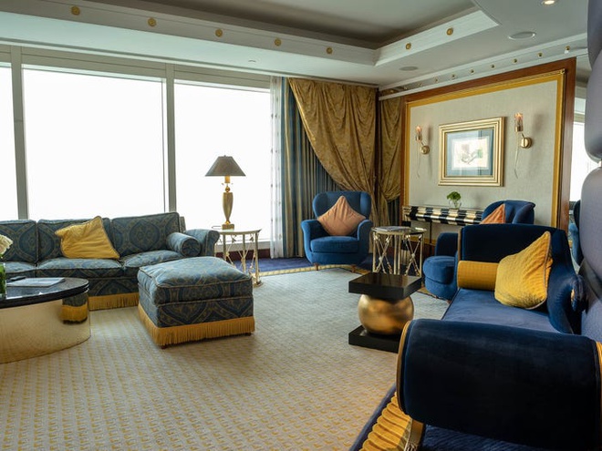 Hình ảnh một phòng khách rộng rãi với cửa sổ kính trong suốt, sofa màu xanh nước biển, họa tiết gấm hoa nổi bật