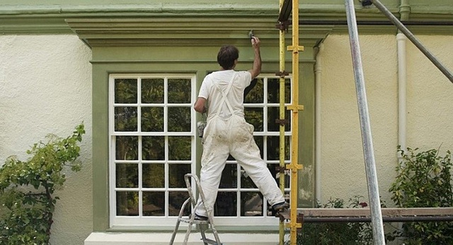 Hình ảnh một người đàn ông luống tuổi đang sơn mặt ngoài ngôi nhà màu xanh lá