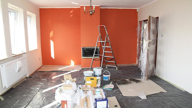 Hình ảnh một căn phòng đang trong quá trình cải tạo, sửa chữa với bức tường màu cam, cửa sổ kính, nền nhà bừa bộn vật liệu