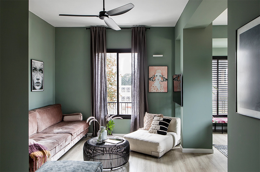 Hình ảnh phòng khách căn hộ đặt cạnh khung cửa sổ kính tron suốt, ghế sofa hồng, bàn trà tròn màu đen, tranh treo tường, cây xanh trang trí