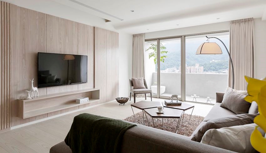 Hình ảnh một phòng khách phong cách tối giản với tường phía sau tivi ốp gỗ, sofa màu trung tính, bàn trà lục giác đặt trên thảm lông, cửa sổ kính trong suốt