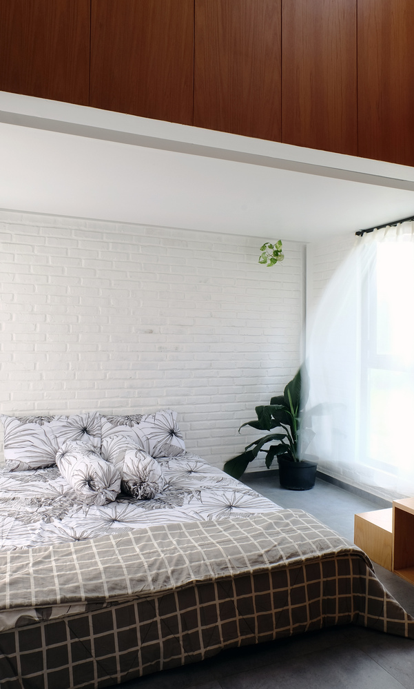 Hình ảnh một phòng ngủ với tường màu tắng, chăn gối kẻ sọc, tủ quần áo bằng gỗ nâu, rèm cửa sổ kính màu trắng