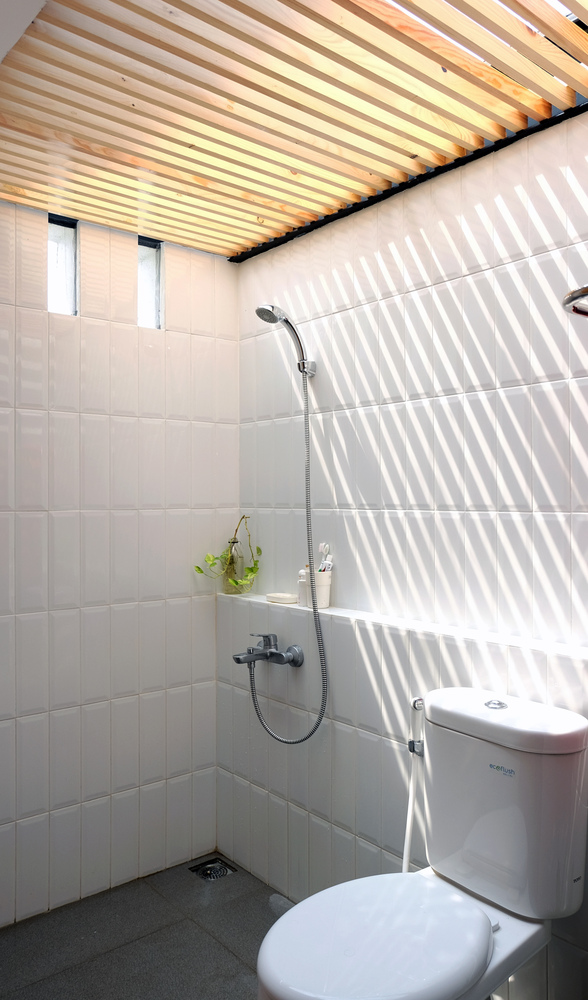 Hình ảnh bên trong một phòng tắm hiện đại với tường, sàn, nội thất màu trắng, trần dầm gỗ tự nhiên