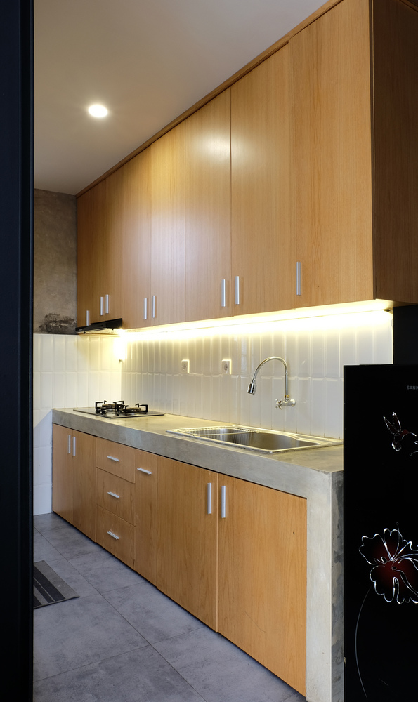 Hình ảnh cận cảnh một góc bếp với hệ tủ lưu trữ bằng gỗ màu sáng có gắn đèn LED, bồn rửa bằng inox