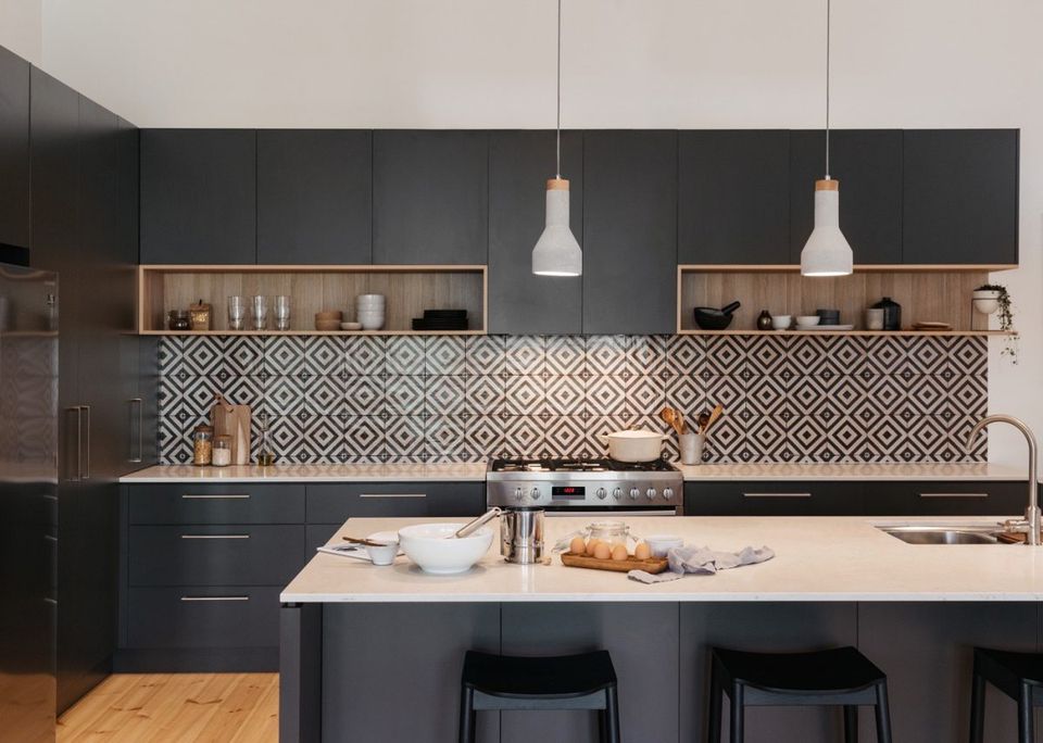 Hình ảnh một phòng bếp hiện đại với tủ bếp màu đen, tường chắn ốp gạch bông họa tiết đen trắng, bàn đảo tiện nghi