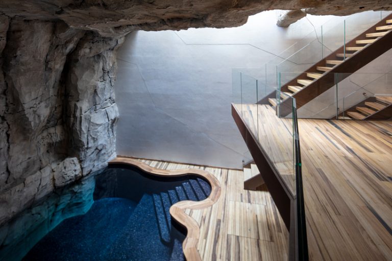 Hình ảnh cầu gỗ dẫn lối vào tầng trệt biệt thự, cạnh đó là bể bơi uốn lướn mềm mại bên vách đá.