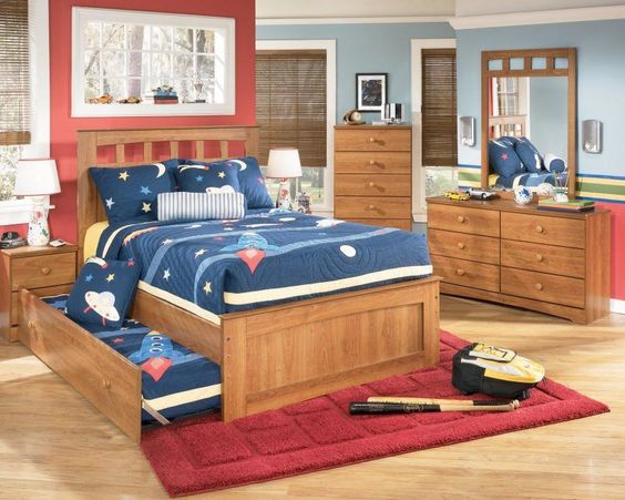 Hình ảnh phòng ngủ dành cho bé trai được trang trí với sắc đỏ đô từ mảng tường đầu giường, thảm trải, chăn gối màu xanh nước biển, quanh đó là hệ tủ lưu trữ bằng gỗ màu sáng