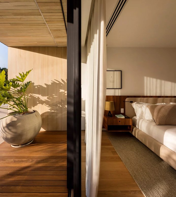 Hình ảnh một góc phòng ngủ trên tầng 2 với cửa kính mở ra ban công trồng cây xanh, trần ốp gỗ