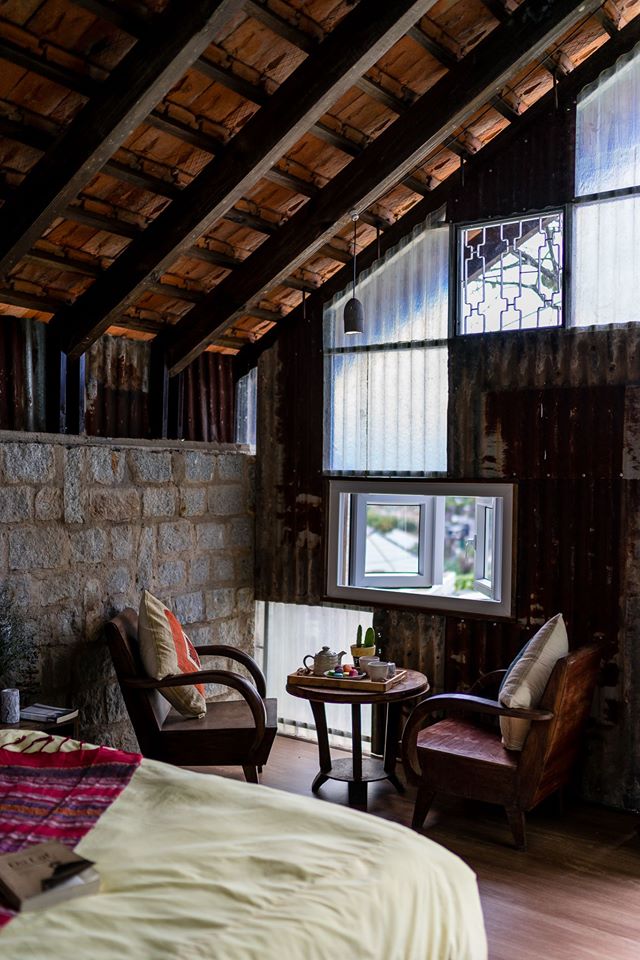 Hình ảnh góc ngồi uống nước, đọc sách trong nhà nghỉ dưỡng với khung cửa sổ kính nhỏ mở ra bên ngoài, tường đá mộc mạc, cạnh đó là giường nệm êm ái