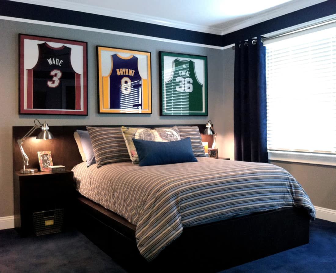 Hình ảnh phòng ngủ của cont rai với chăn ga kể sọc, tranh treo tường họa tiết cầu thủ, cửa sổ kính trong suốt, rèm và thảm màu xanh dương