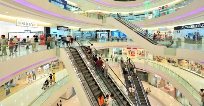 Hình ảnh bên trong một trung tâm thương mại với mặt bằng bản lẻ trải đều các tầng, thang máy, khách hàng đang mua sắm