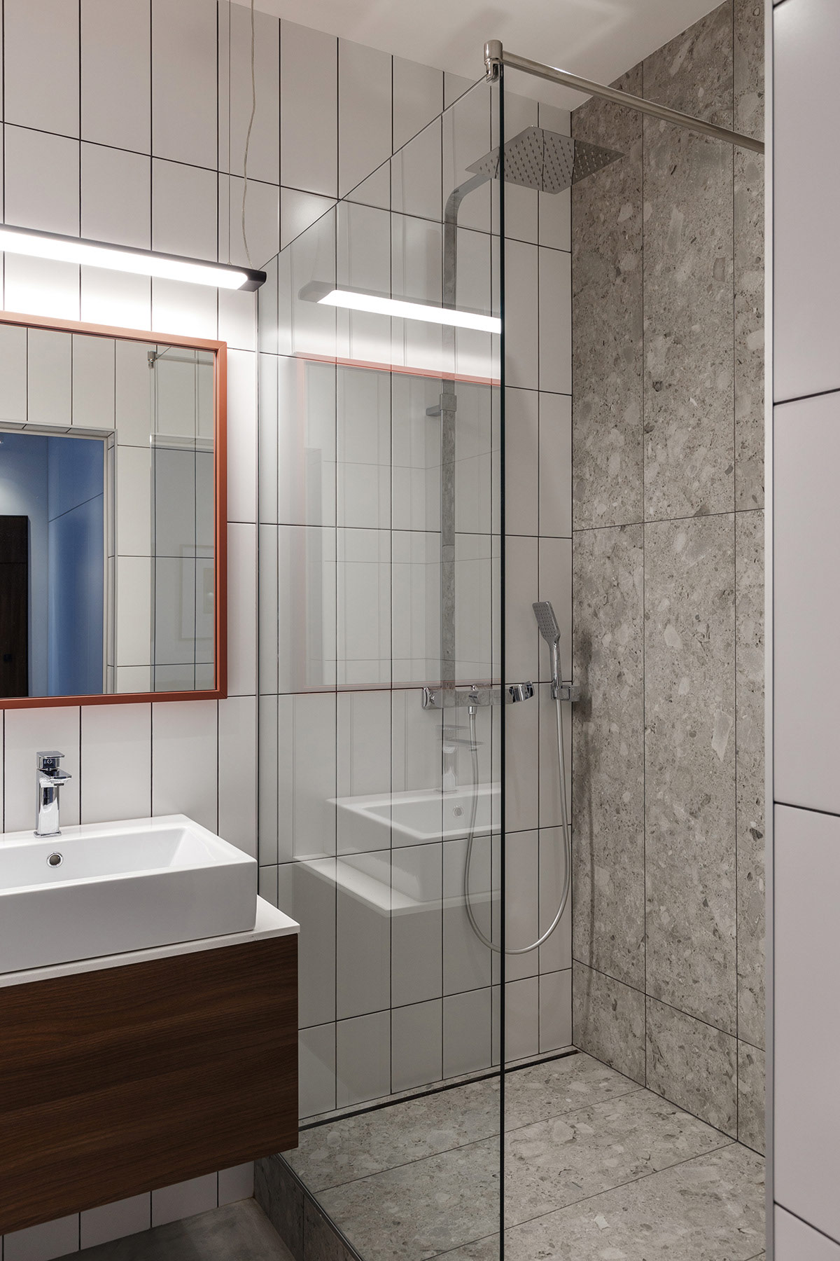 Hình ảnh phòng tắm với tường ốp gạch men màu trắng, xám sạch sẽ, vách kính trong suốt, gương lớn treo tường