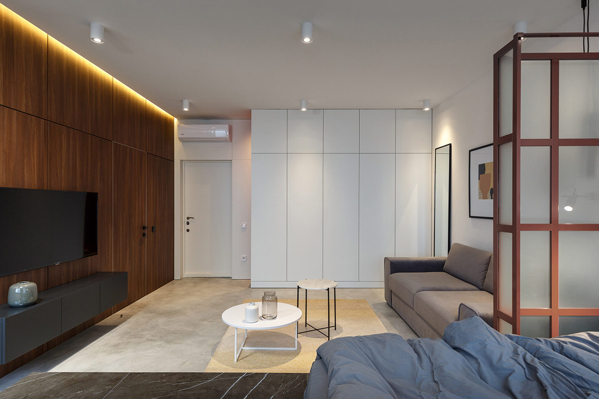 Hình ảnh toàn cảnh không gian sinh hoạt chung trong căn hộ nhỏ với sofa màu xám, kệ tivi, tủ lưu trữ âm tường màu trắng